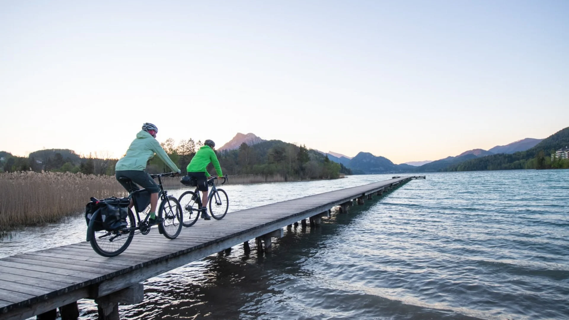 Two cyclists on a pier by the lake with mountains in the background