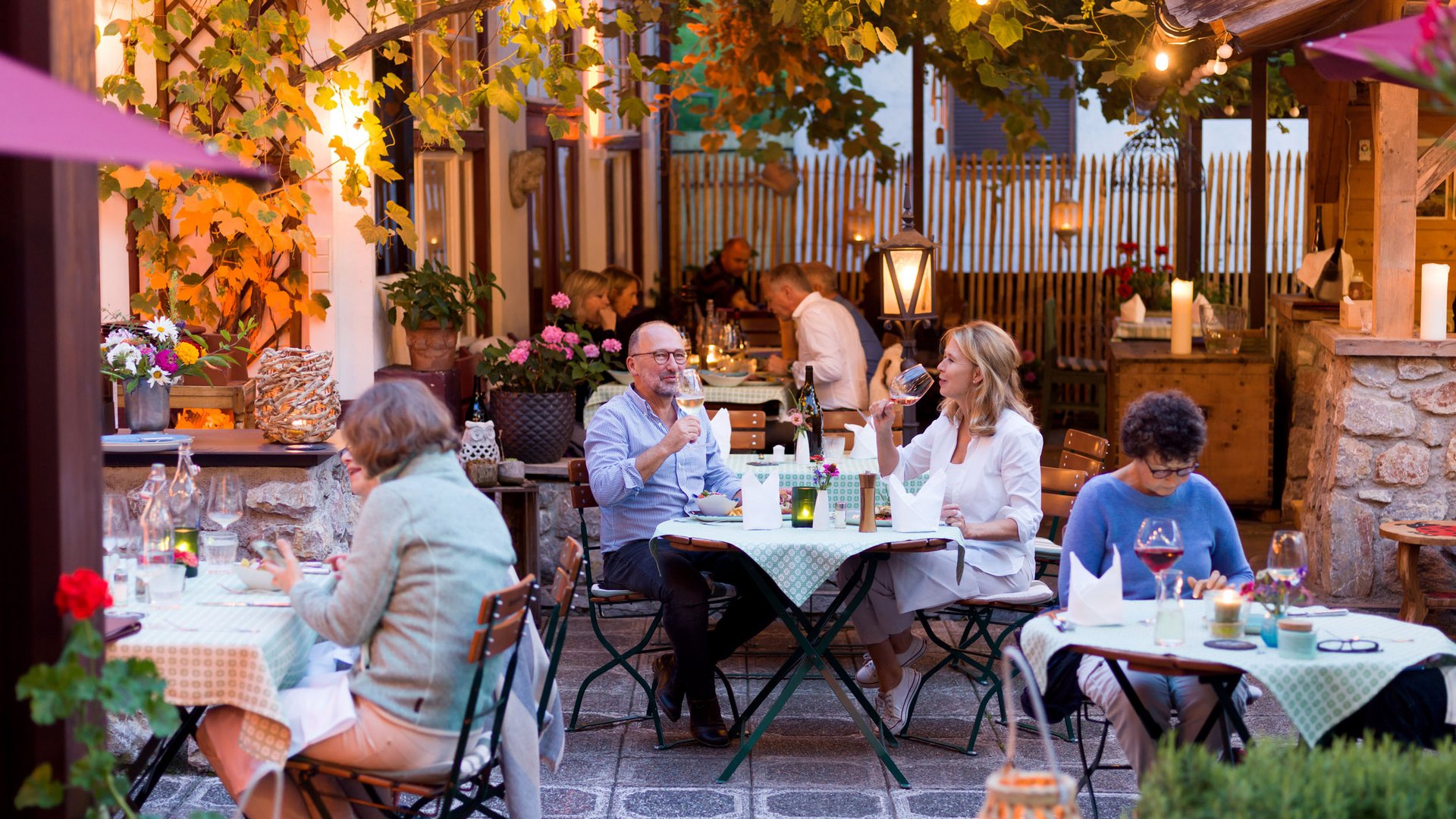 People dining outdoors in cozy restaurant setting with wine and warm lights