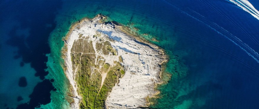 Aerial view of a rocky peninsula with green vegetation surrounded by blue sea