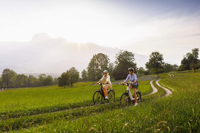 Zwei Frauen fahren mit dem Fahrrad auf einem Feldweg bei sonnigem Wetter