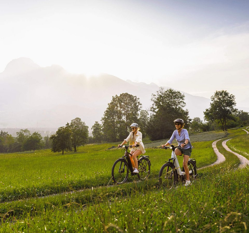 Zwei Frauen fahren mit dem Fahrrad auf einem Feldweg bei sonnigem Wetter