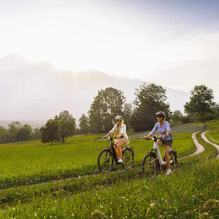 Zwei Frauen fahren mit dem Fahrrad auf einem Feldweg bei sonnigem Wetter