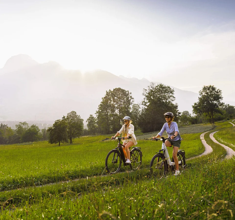 Zwei Frauen fahren mit dem Fahrrad auf einem Feldweg bei sonnigem Wetter
