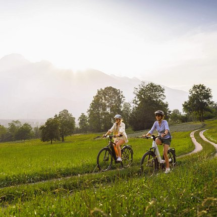 Zwei Frauen fahren mit dem Fahrrad auf einem Feldweg bei sonnigem Wetter