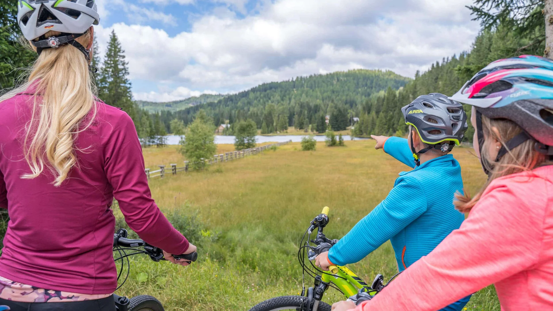 Familie mit Fahrrädern genießt Aussicht auf Wald und See bei sonnigem Wetter