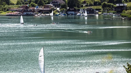 Kulinarisch unterwegs in Tramin © IDM Südtirol - Benjamin Pfitscher Segelboot auf glitzerndem See vor grünen Weinbergen und Häusern