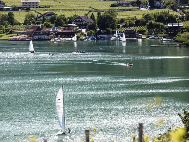 Kulinarisch unterwegs in Tramin © IDM Südtirol - Benjamin Pfitscher Segelboot auf glitzerndem See vor grünen Weinbergen und Häusern