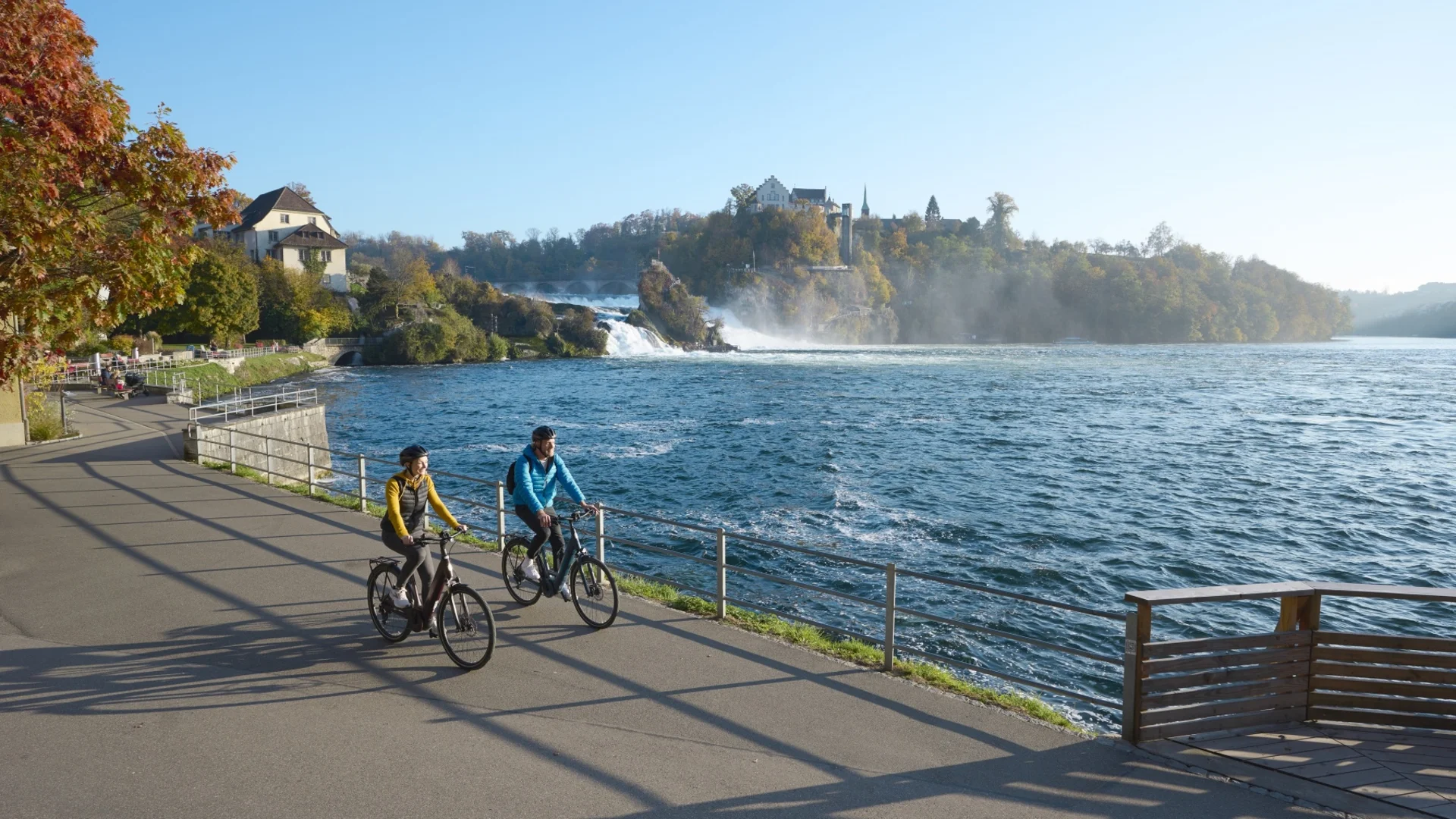 Twee fietsers bij de Rijnwaterval met kasteel en waterval op de achtergrond