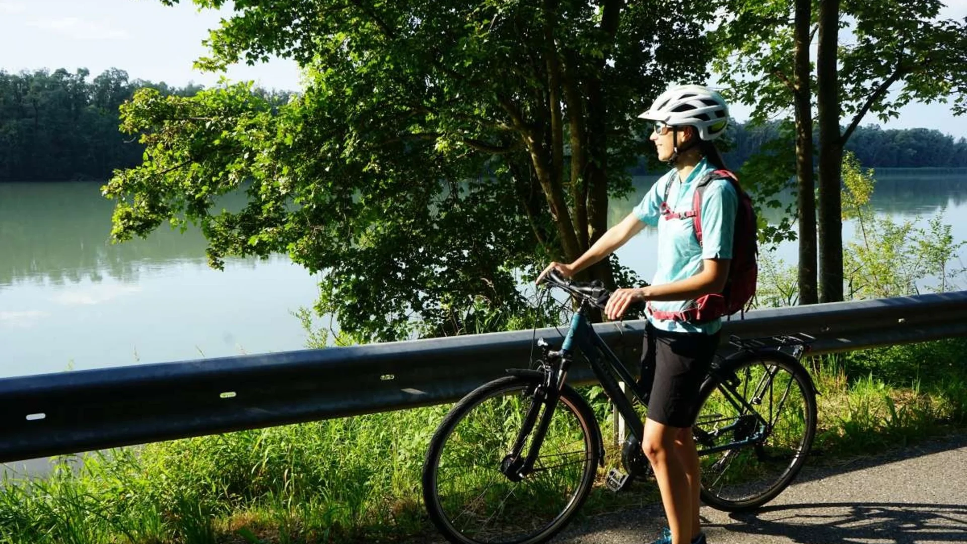 Frau mit Helm auf Fahrrad hält an See an, um die Aussicht zu genießen