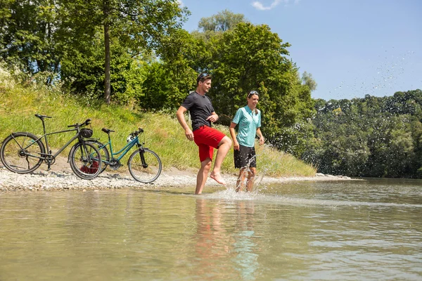 Die schönsten Radregionen im Süden Deutschlands © Velontour Zwei Menschen planschen mit Fahrrädern am Flussufer im Sommer
