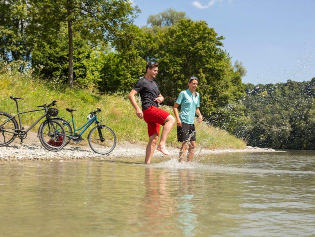 Zwei Menschen planschen mit Fahrrädern am Flussufer im Sommer