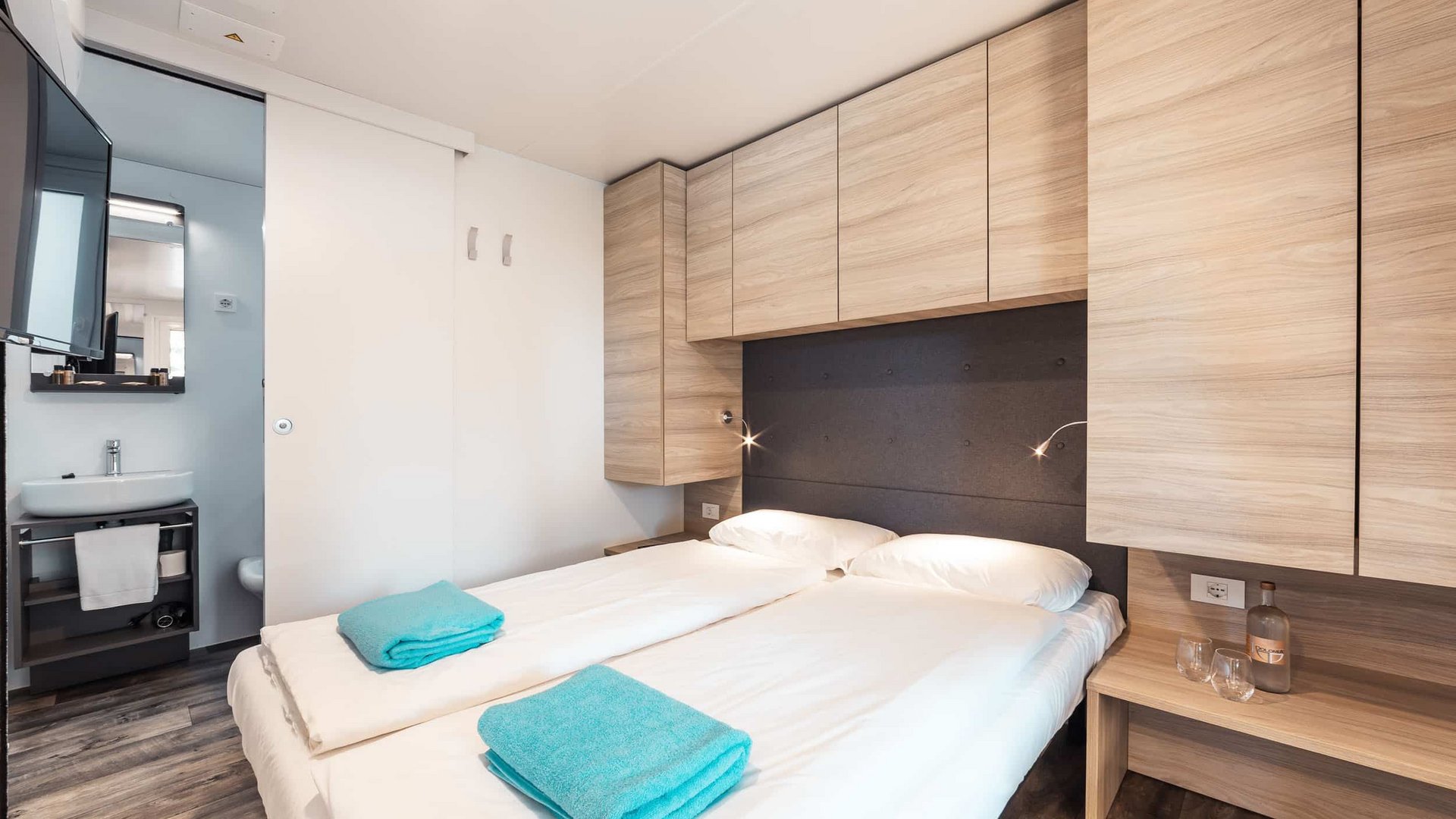 Small modern bedroom with two beds, wooden cabinets, and a bathroom