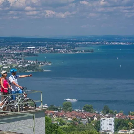 Zwei Radfahrer auf Balkon mit Blick auf See und Stadt