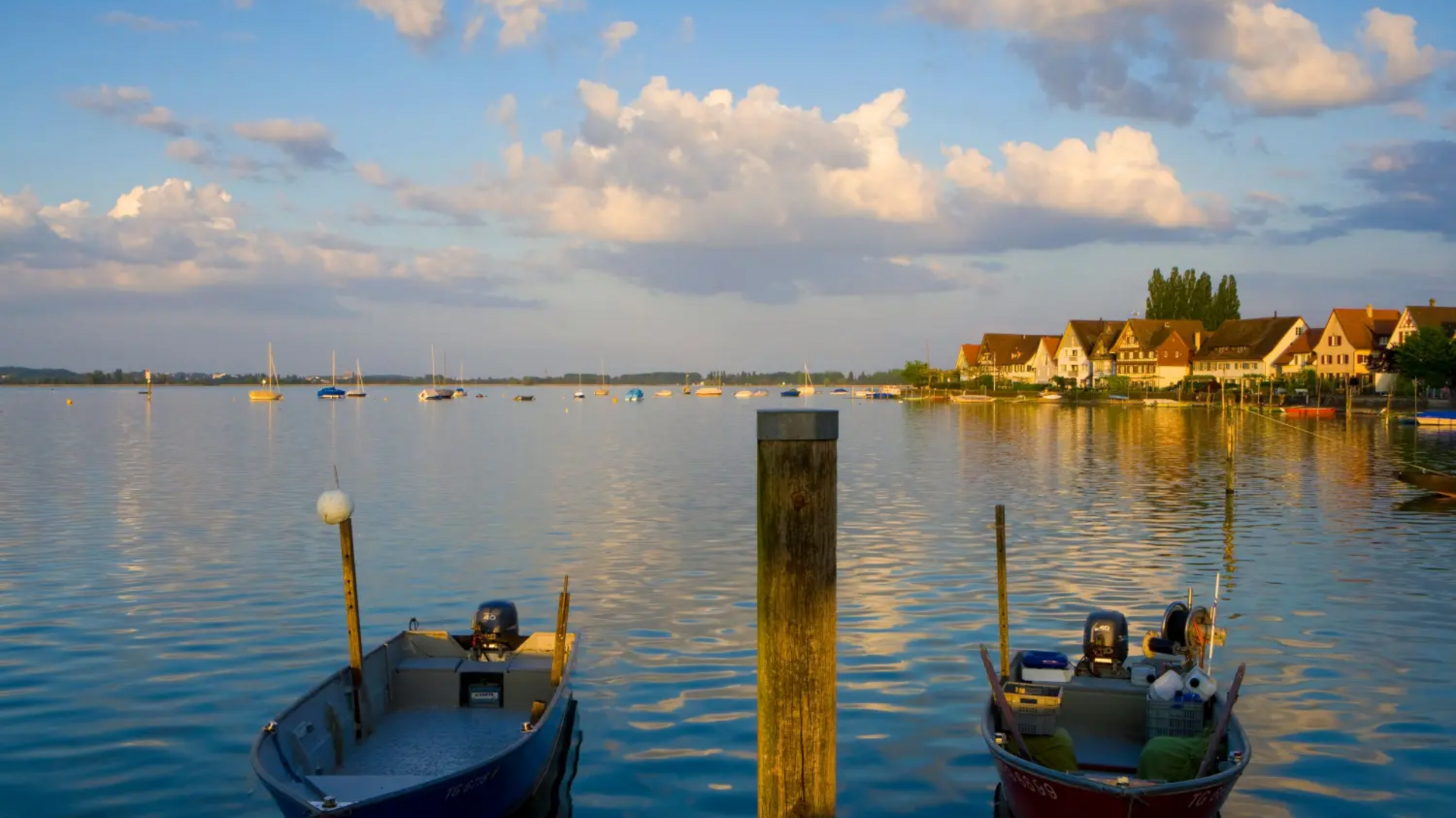 Two boats on calm lake at sunset with houses along the shore