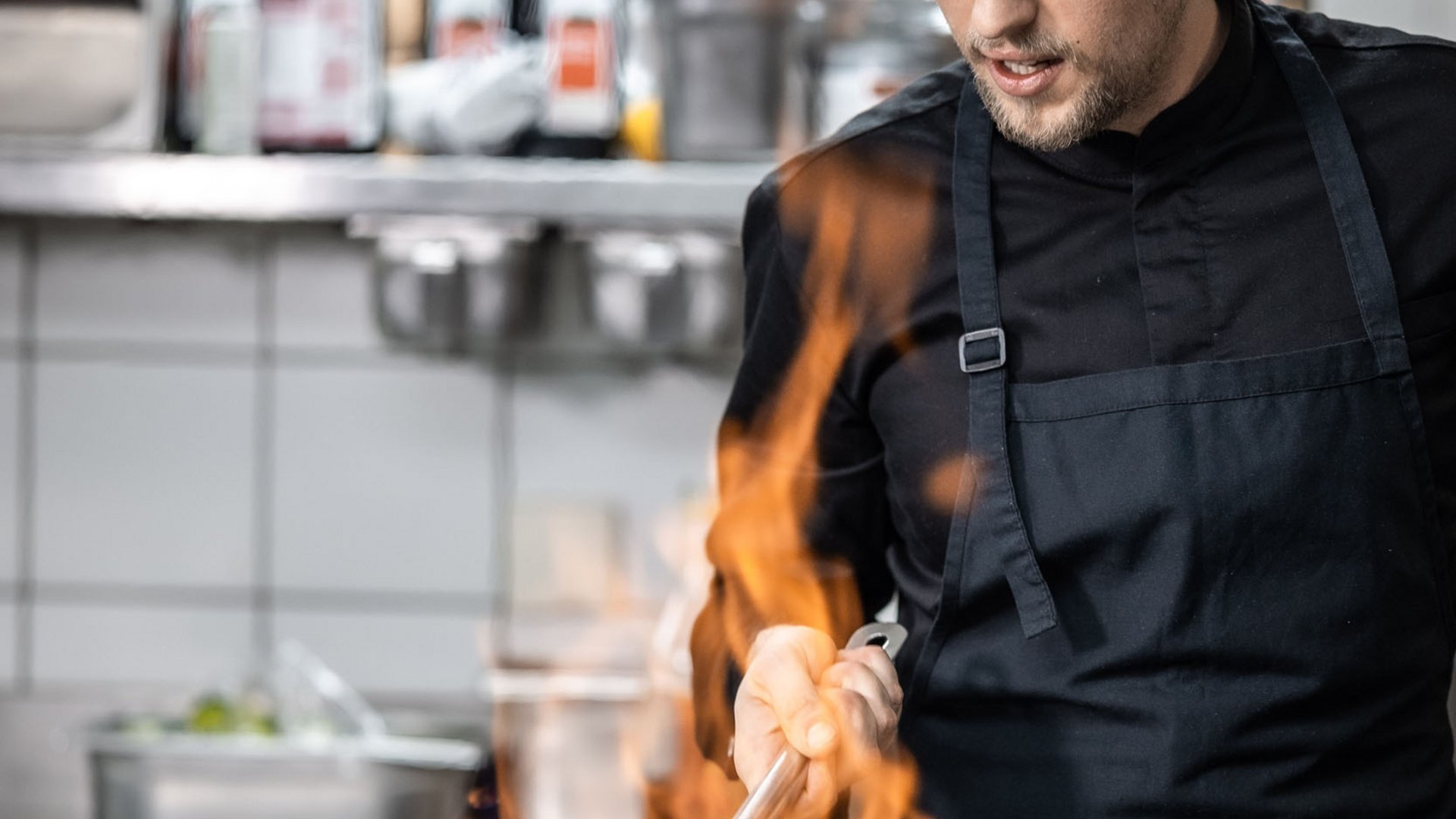 Chef cooking vegetables with flames in a pan in commercial kitchen