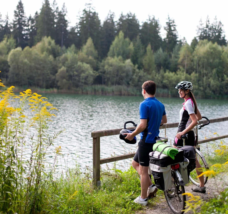 Zwei Radfahrer stehen am Seeufer und genießen die Aussicht
