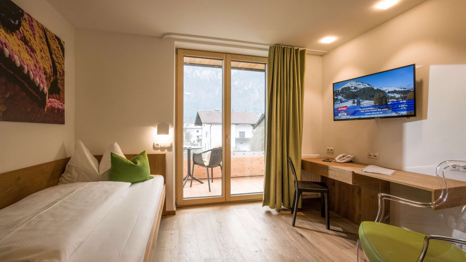 Modern hotel room with balcony, single bed, TV and desk