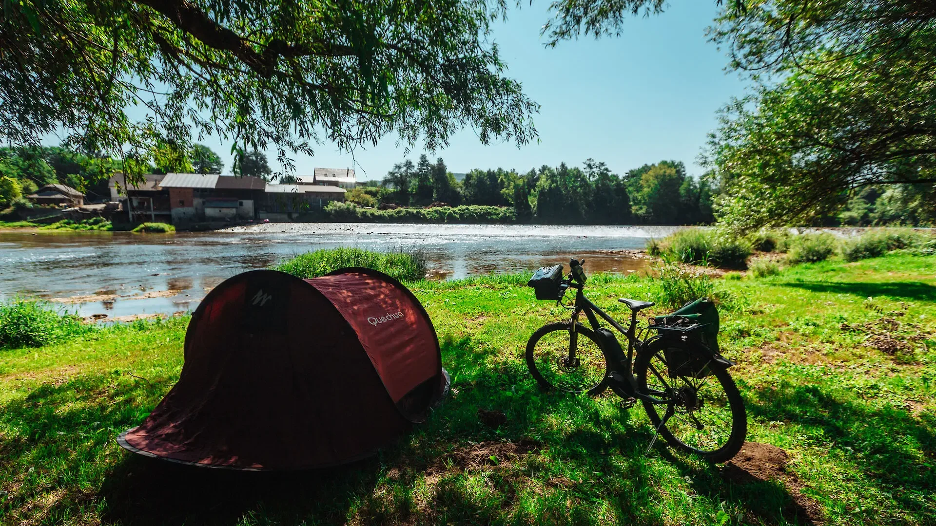 Tent en fiets bij de rivier onder bomen op een zonnige dag
