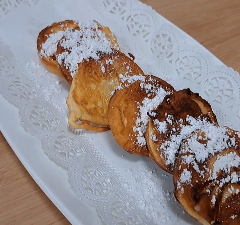 Five fried apple slices with powdered sugar on a white plate