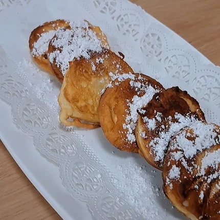 Vijf gebakken appelschijfjes met poedersuiker op een wit bord
