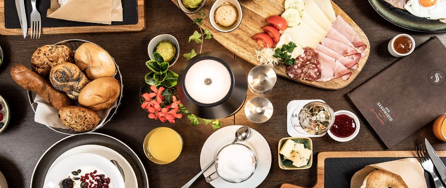 Breakfast table with rolls, cold cuts, eggs, and drinks