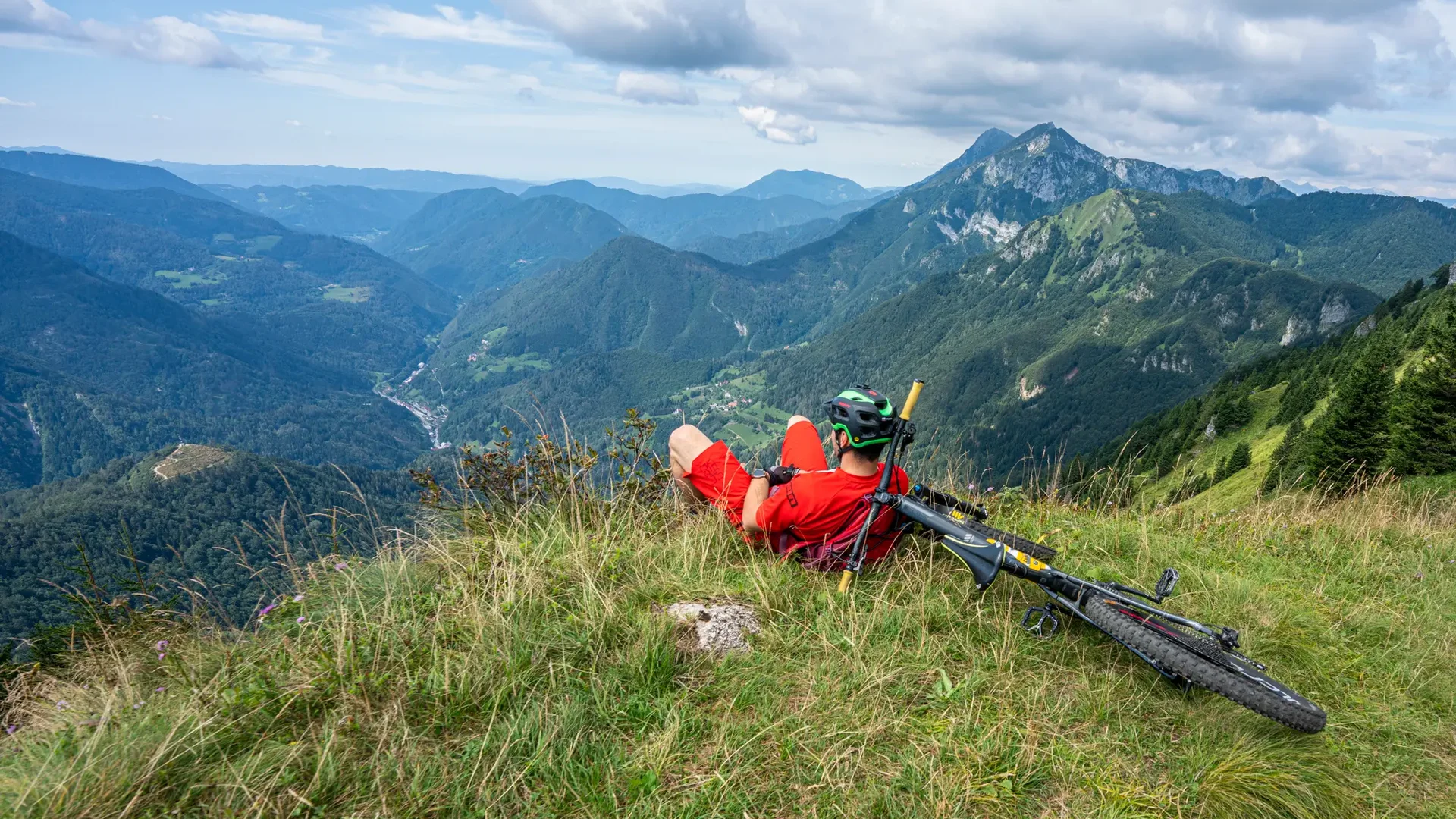 Mountainbiker rust op berg met uitzicht op groene valleien en bewolkte lucht
