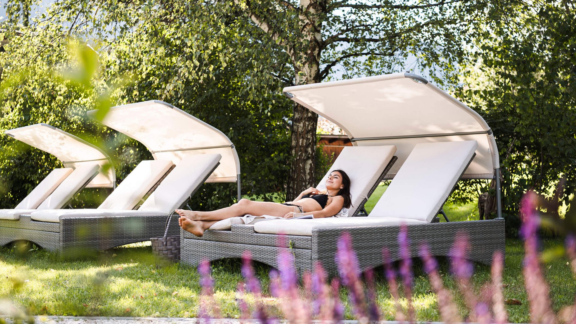 Woman relaxing on sun lounger in garden with trees and sunlight