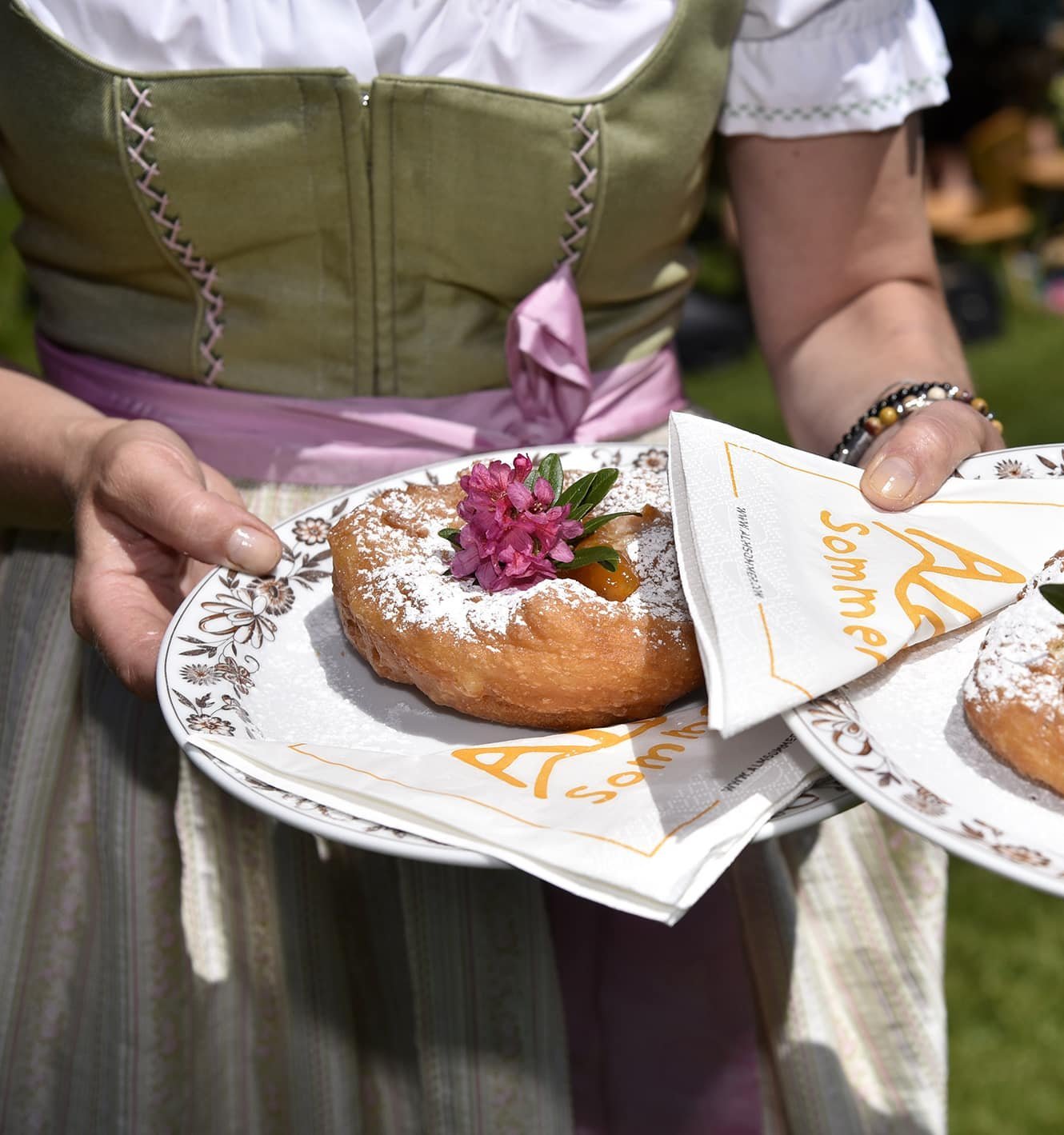 Person holding plates with traditional cake topped with powdered sugar and flower