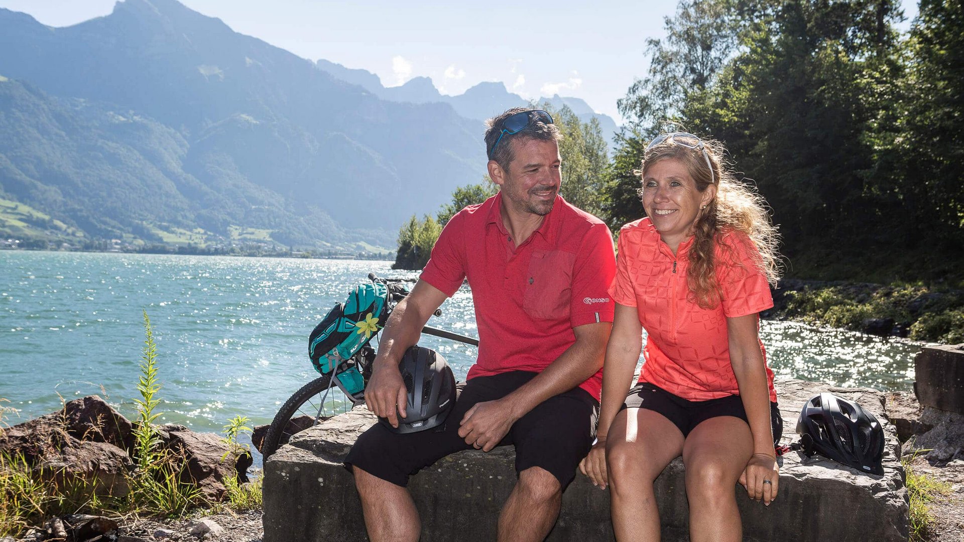 Mann und Frau in Sportkleidung machen Pause am See mit Bergen im Hintergrund