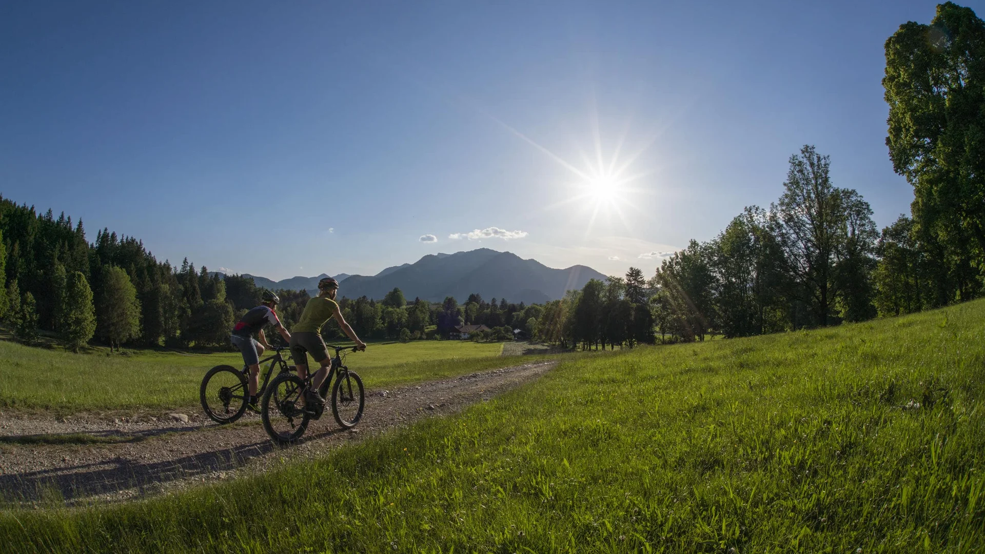 Im Sattel durchs Tölzer Land entlang von Isar & Loisach © Tölzer Land Tourismus - Bernd Ritschel Zwei Radfahrer auf einem Weg in grüner Landschaft bei Sonnenschein