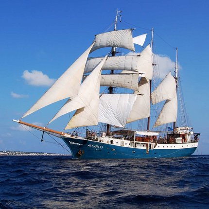 Sailing ship Atlantis with white sails on blue sea under clear sky