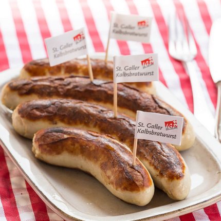 Grilled St. Galler veal sausages on a plate with fork and knife