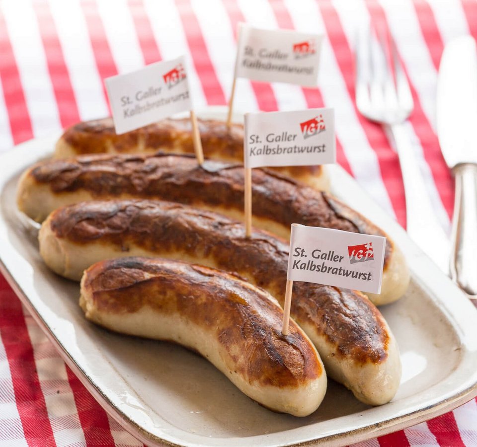Grilled St. Galler veal sausages on a plate with fork and knife