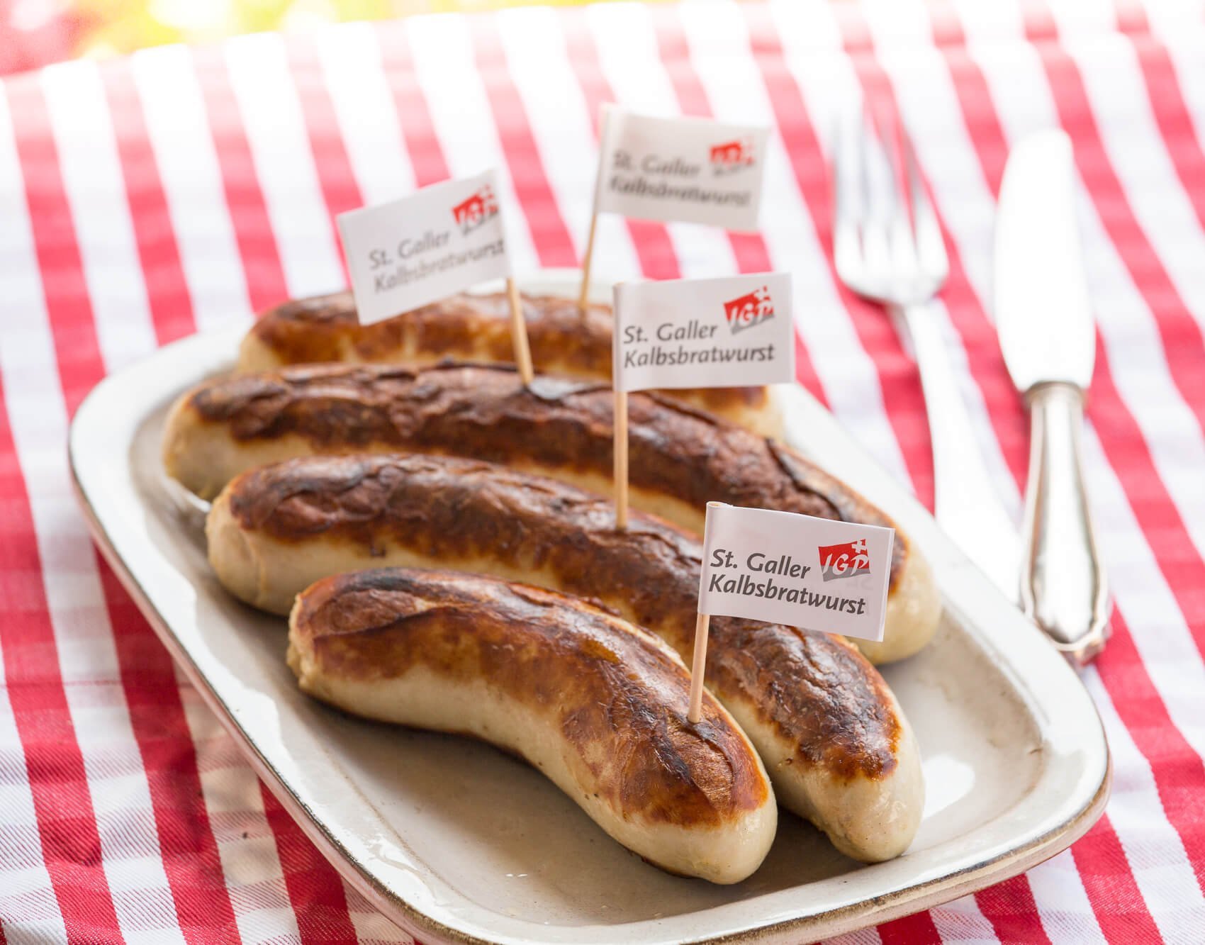 Grilled St. Galler veal sausages on a plate with fork and knife