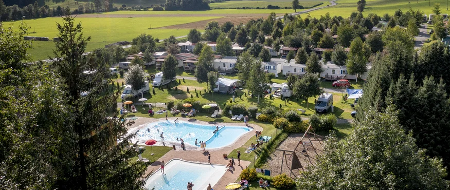 Camping in een dal met bergen, bomen en zwembaden onder een bewolkte lucht
