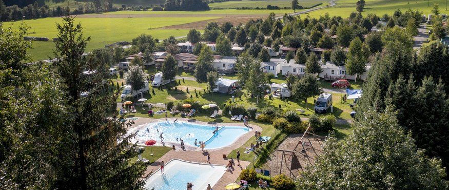 Campsite in a valley with mountains, trees, and pools under cloudy sky