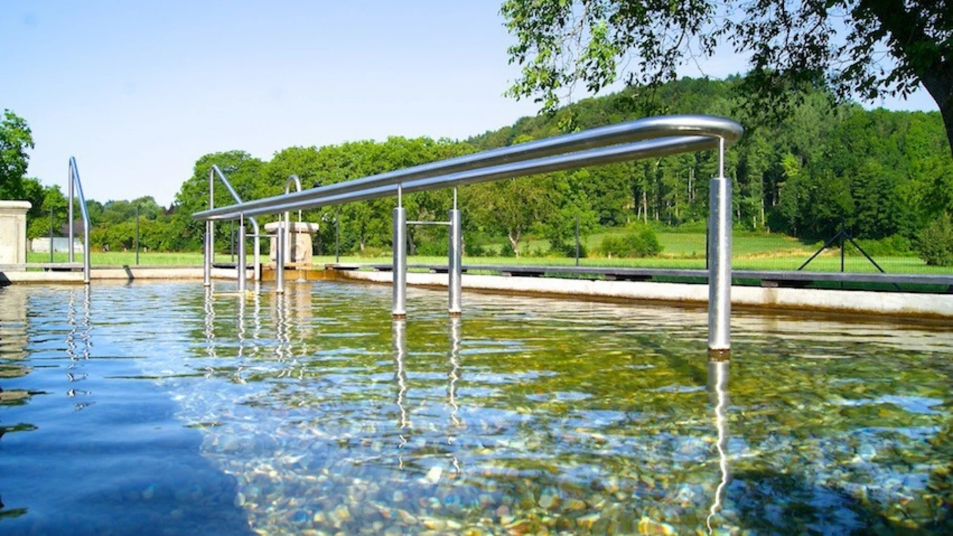 Kneipp-Becken mit klarem Wasser und Metalldurchlauf in grüner Landschaft