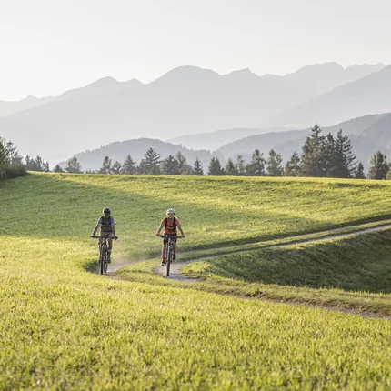 Twee fietsers op een pad door groene velden met bergen op de achtergrond