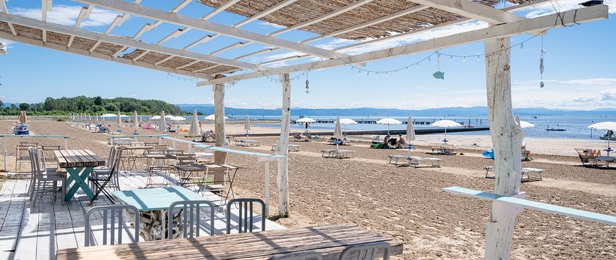 Beach bar with wooden tables and chairs next to sandy beach and umbrellas