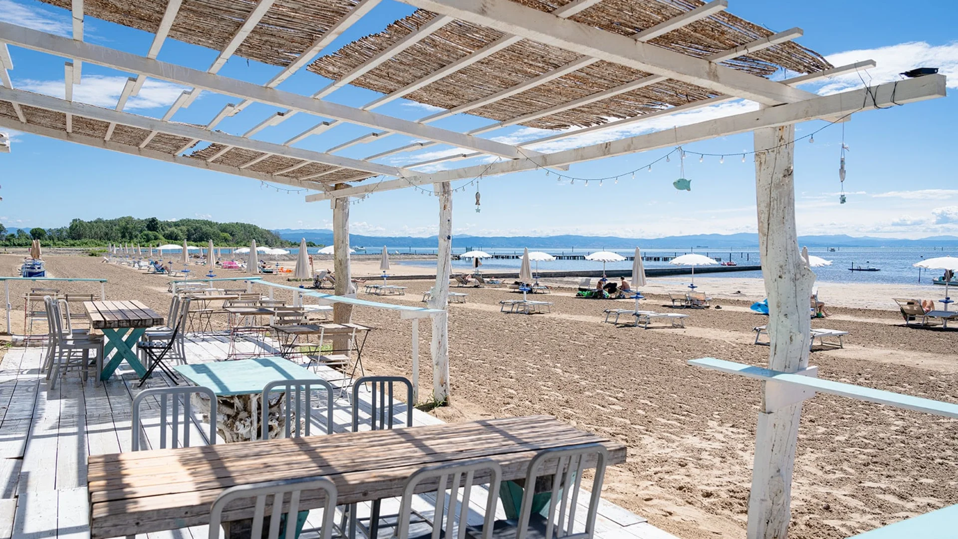 Beach bar with wooden tables and chairs next to sandy beach and umbrellas