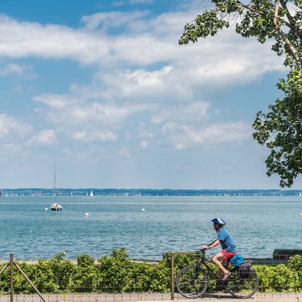 Cyclist by the lakeside with sailboats and partly cloudy sky