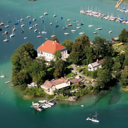Aerial view of a wooded island with buildings and sailboats in clear water