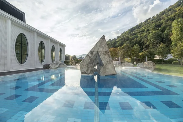 Heidiland: Von Wein bis Thermalwasser © Tamina Therme Bad Ragaz Außenpool mit geometrischer Marmor-Skulptur neben weißem Gebäude und Waldhügel
