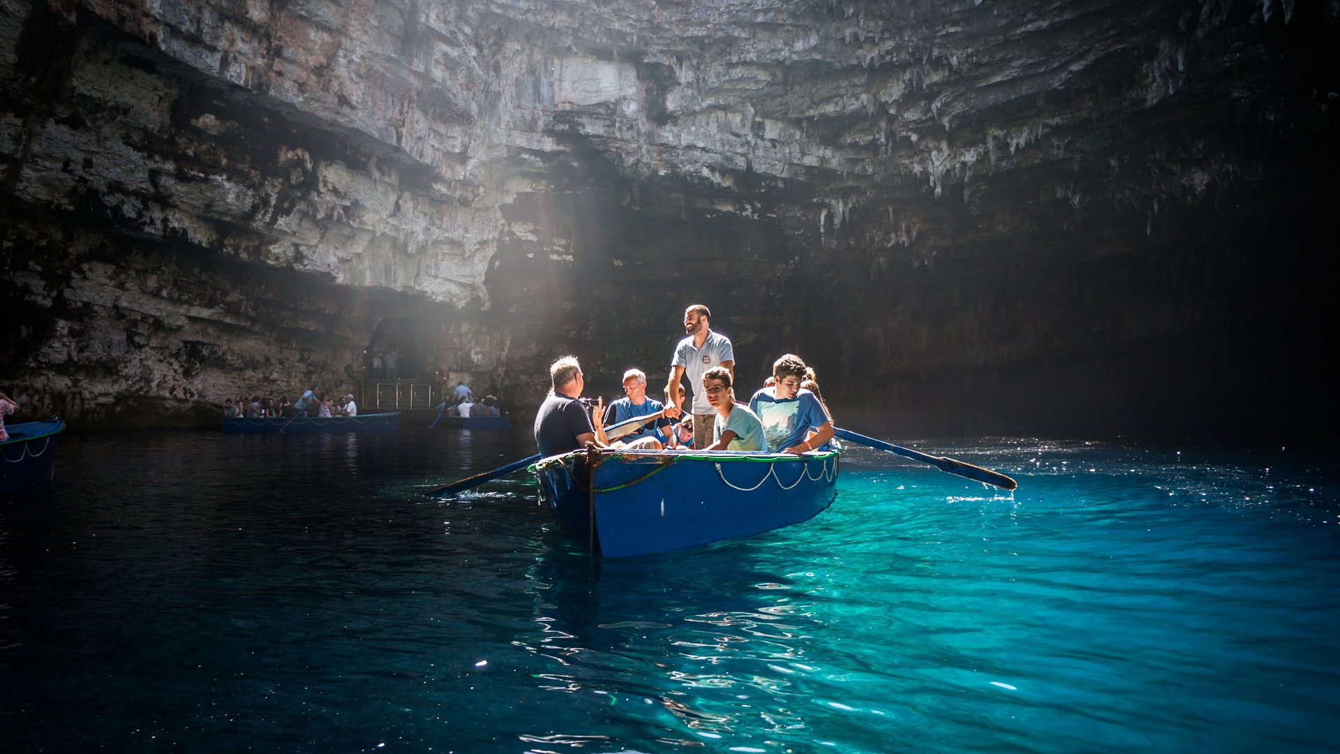 People in a boat on clear water inside a large cave