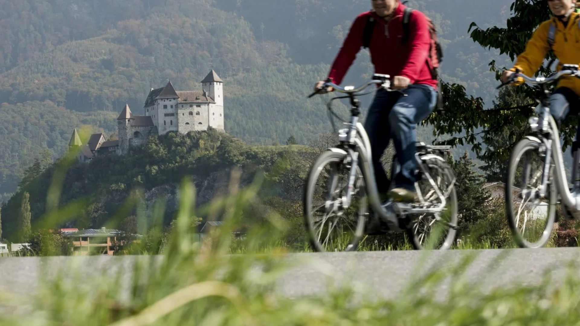 Zwei Radfahrer vor einer Burg auf einem grünen Hügel
