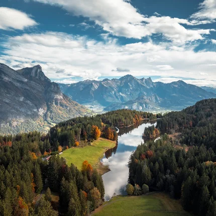 Herbstliche Berglandschaft mit Fluss und bewaldeten Hügeln unter bewölktem Himmel