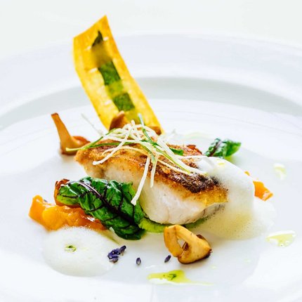 Gourmet fish fillet with vegetables and foam on a white plate
