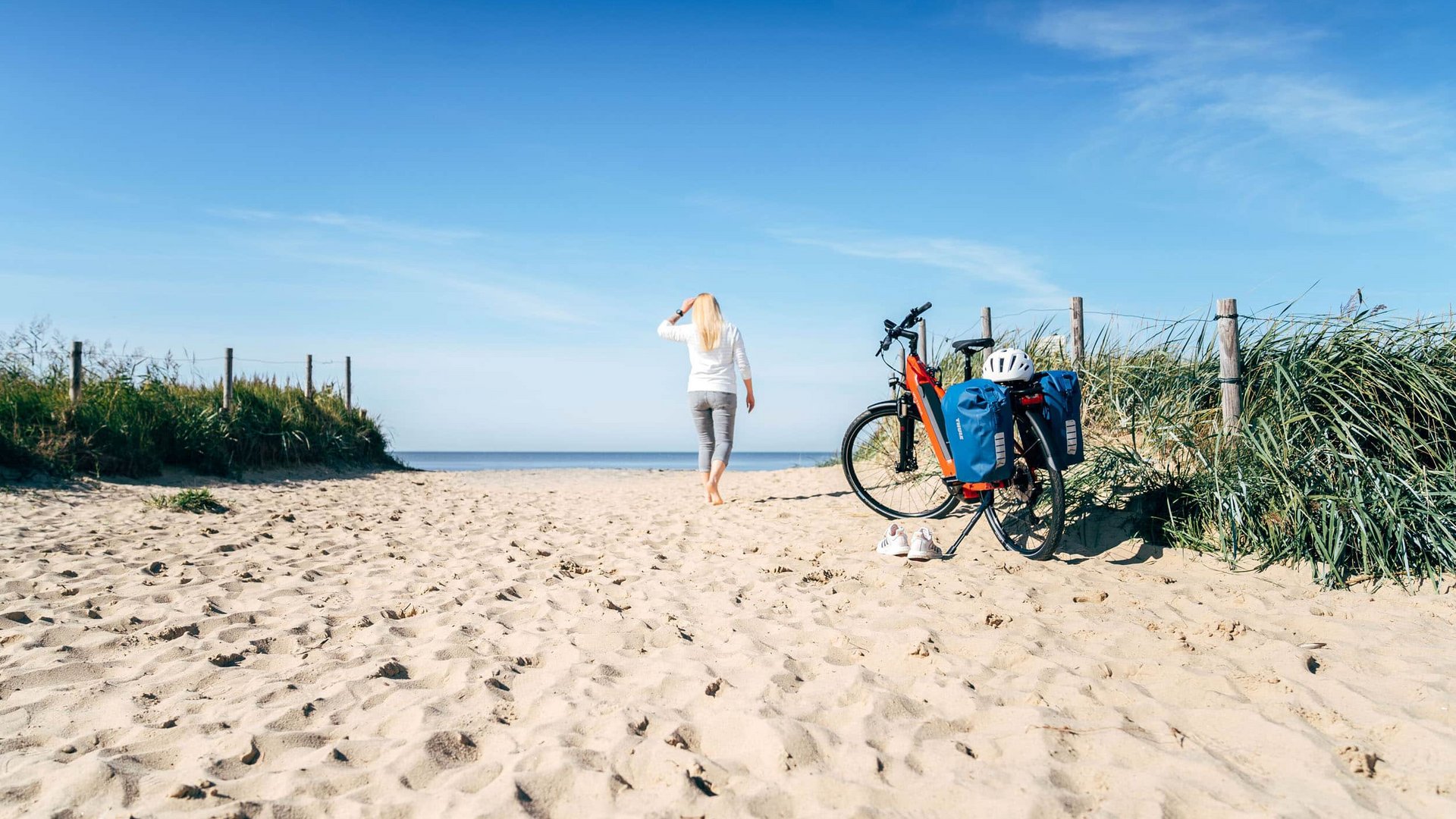 Victoria Woman walks barefoot to the sea, bicycle with bags in the sand
