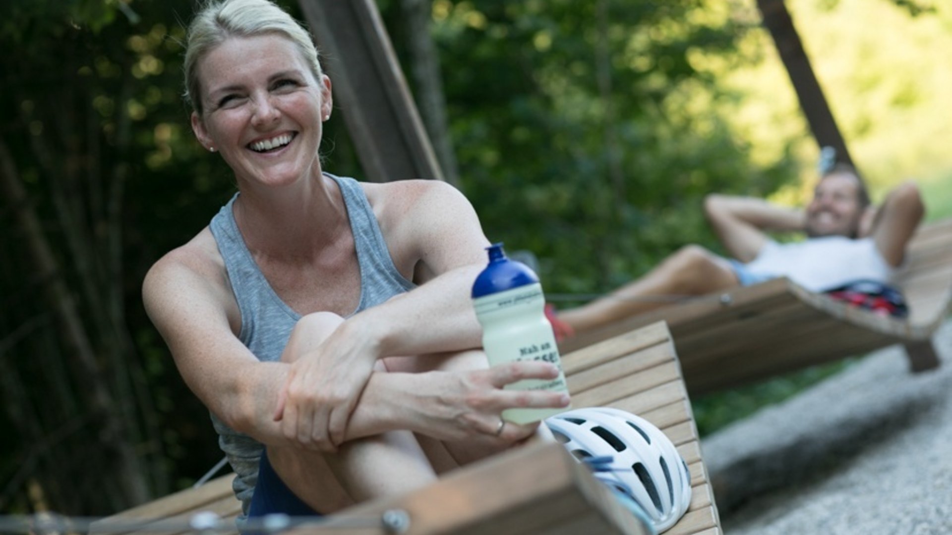 Woman holding water bottle relaxing outdoors on a wooden lounge chair