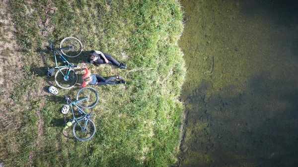 Aufsatteln und genießen in Oberbayern © Tourismus Oberbayern München - Tobias Köhler Zwei Radfahrer sitzen auf Gras am Ufer eines Gewässers mit ihren Fahrrädern